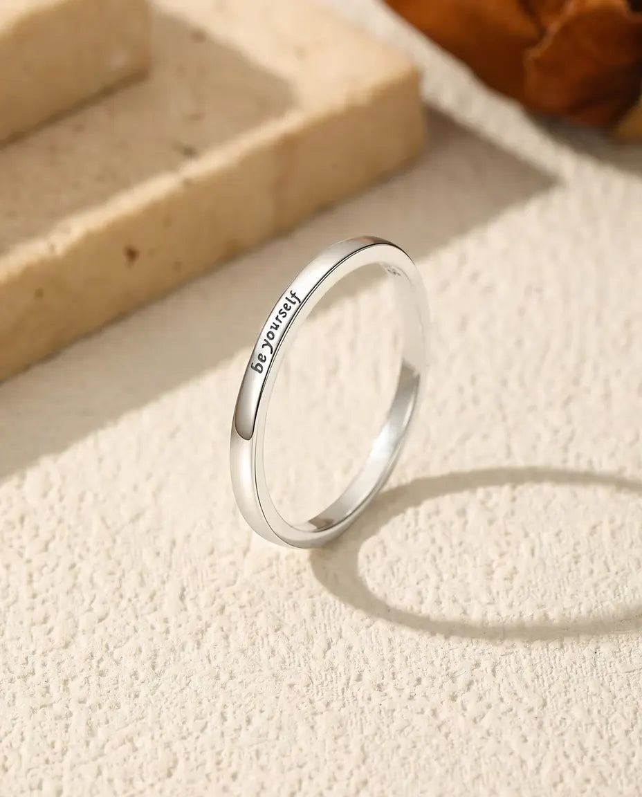Bague Gravée « be yourself » en Argent 925 - posée debout sur une surface claire texturée