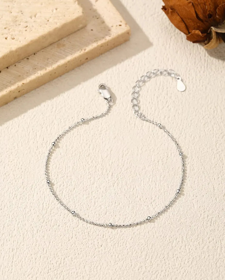 Bracelet Chaîne Boules en Argent 925 - posé à plat sur une surface claire texturée, avec fermoir et chaînette d’extension