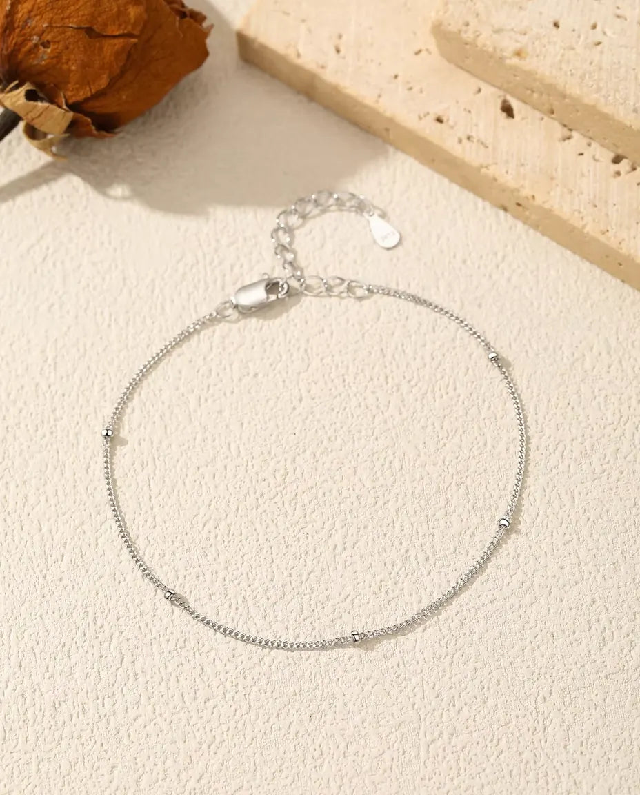 Bracelet Chaîne Satellite en Argent 925 - posé à plat sur une surface claire texturée, avec fermoir et chaînette d’extension