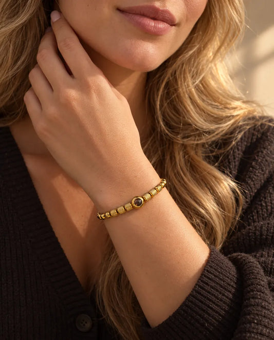 Femme effleurant son cou, portant le bracelet doré à perles texturées et photo cachée