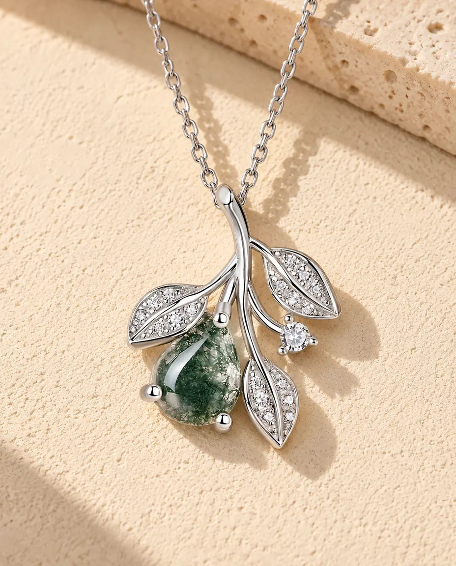 Collier Agate Mousse Feuilles en Argent 925 - posé sur une surface claire texturée près d’un bloc de travertin