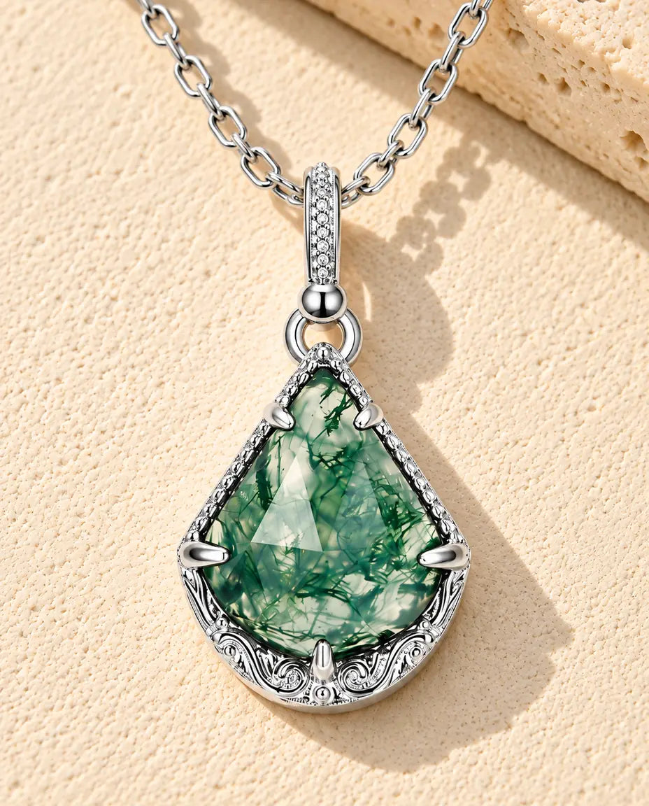 Collier Agate Mousse Écusson en Argent 925 - posé sur une surface claire texturée près d’un bloc de travertin