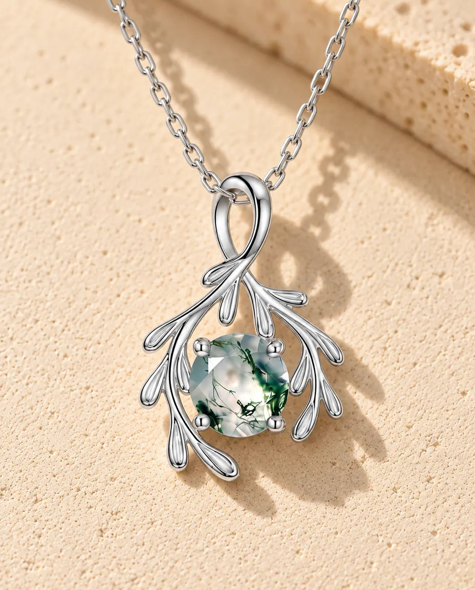 Collier Agate Mousse Branche en Argent 925 - posé sur une surface claire texturée près d’un bloc de travertin