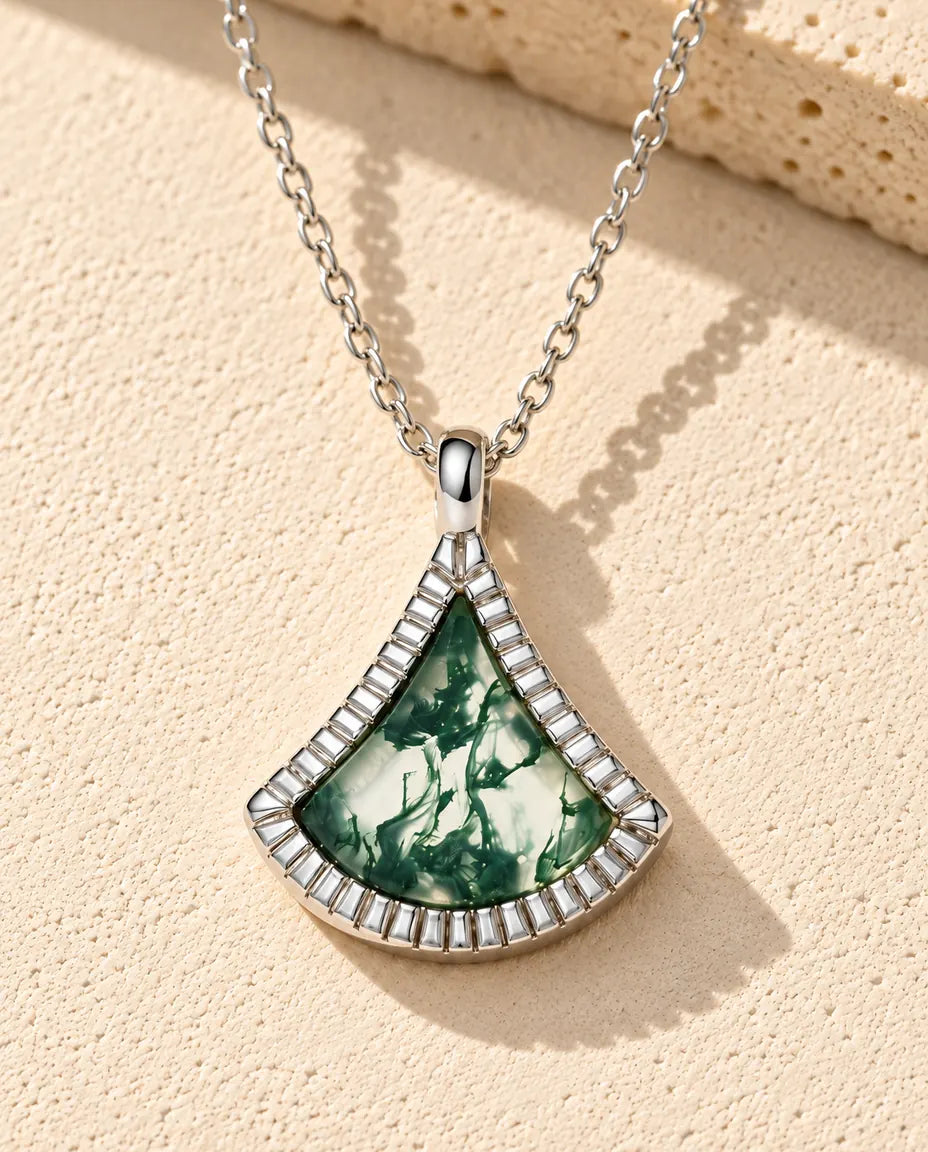 Collier Agate Mousse Éventail en Argent 925 - posé sur une surface claire texturée près d’un bloc de travertin