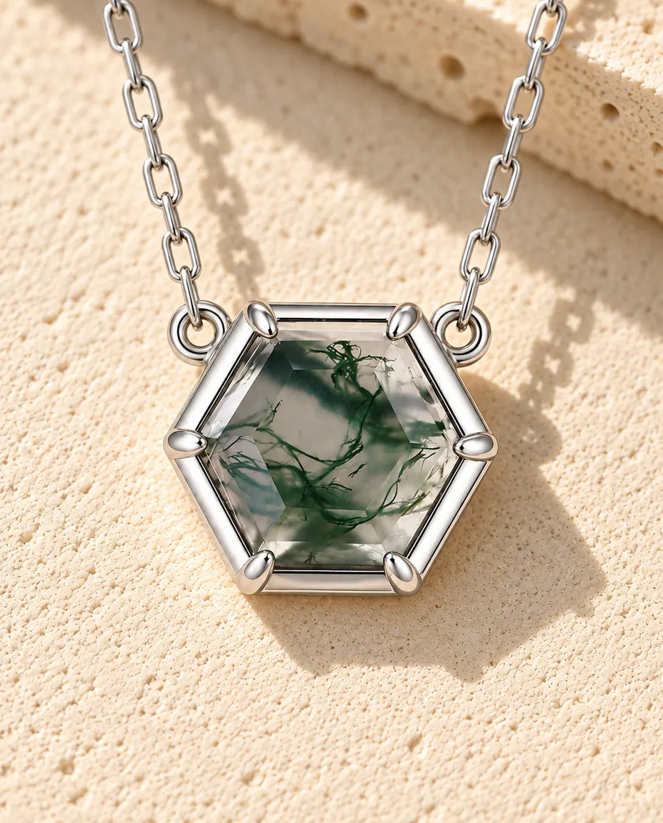 Collier Agate Mousse Hexagonale en Argent 925 - posé sur une surface claire texturée près d’un bloc de travertin