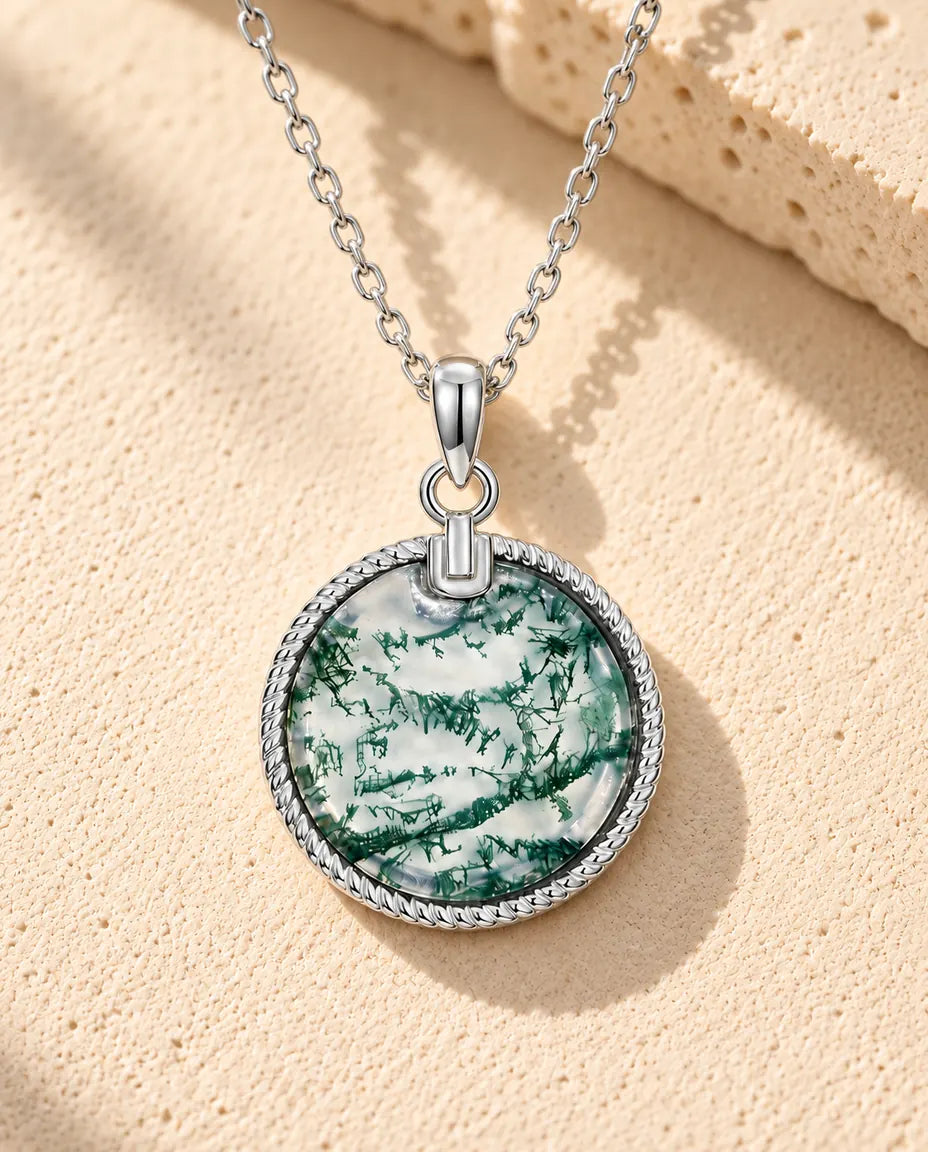 Collier Agate Mousse Médaillon Rond en Argent 925 - posé sur une surface claire texturée près d’un bloc de travertin