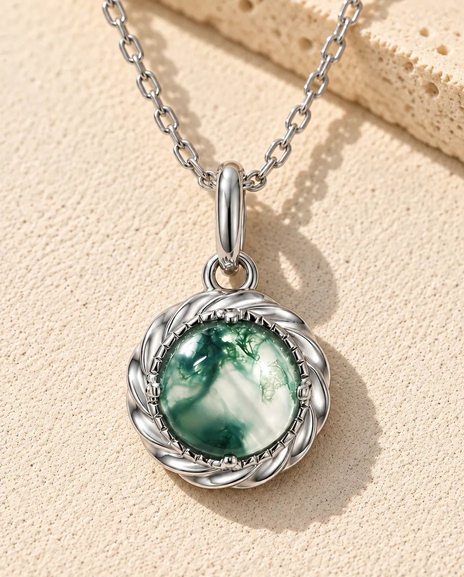 Collier Pendentif Agate Mousse Ronde en Argent 925 - posé sur une surface claire texturée près d’un bloc de travertin