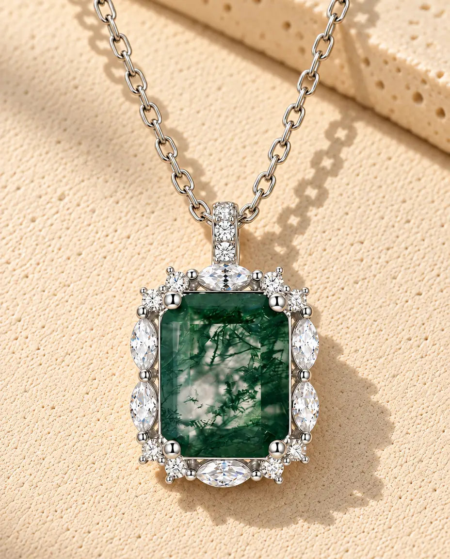 Collier Agate Mousse Taille Émeraude en Argent 925 - posé sur une surface claire texturée près d’un bloc de travertin