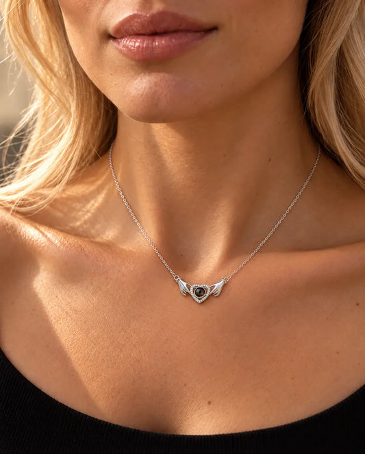Femme en haut en maille noir portant le collier argenté aux deux mains tenant un cœur avec photo