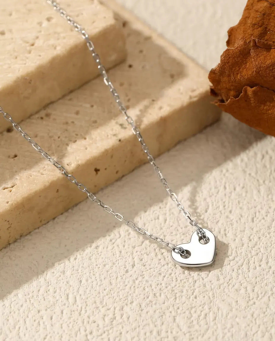 Collier Cœur en Argent 925 - pendentif posé sur une surface claire près d’une dalle de travertin