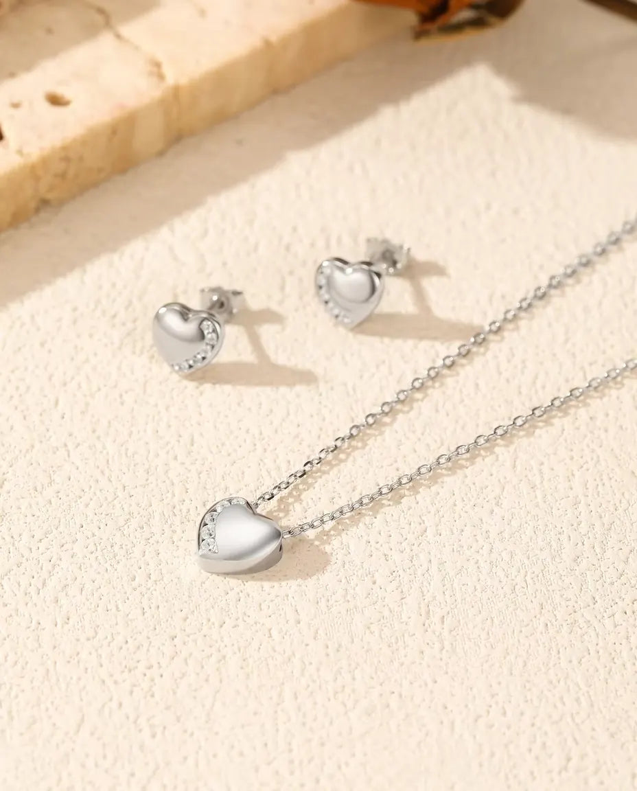 Parure Cœur en Argent 925 - collier et boucles d’oreilles posés ensemble sur une surface claire texturée