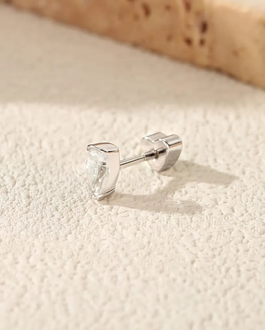 Puces d’Oreilles Moissanite Poire en Argent 925 - posée sur une surface claire texturée près d’une dalle de travertin