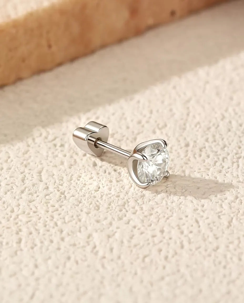 Puces d’Oreilles Solitaire Moissanite 5 mm Quatre Griffes en Argent 925 - posée sur le côté sur une surface claire texturée, fermoir en forme de cœur sur la tige