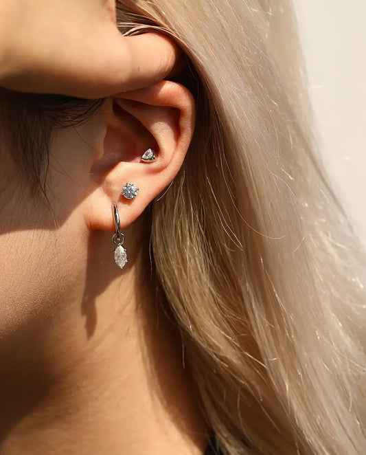 Puces d’Oreilles Solitaire Moissanite 5 mm Quatre Griffes en Argent 925 - portée par un mannequin qui dégage ses cheveux derrière l’oreille