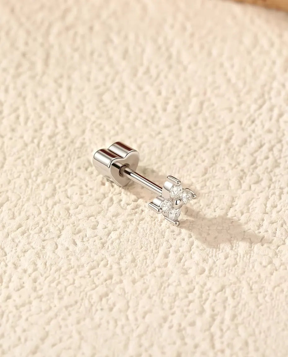 Puces d’Oreilles Trèfle à Quatre Feuilles Moissanite en Argent 925 - posée sur le côté sur une surface claire texturée, fermoir en forme de cœur sur la tige