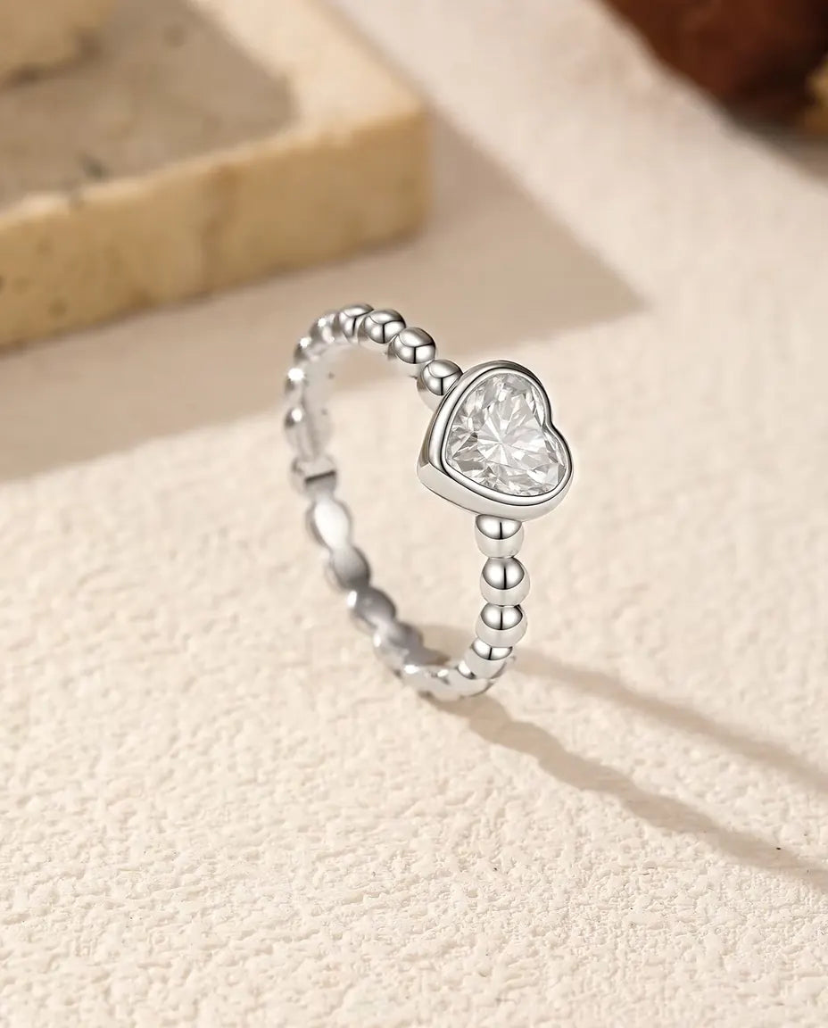 Bague Cœur Moissanite en Argent 925 - posée debout sur une surface claire texturée