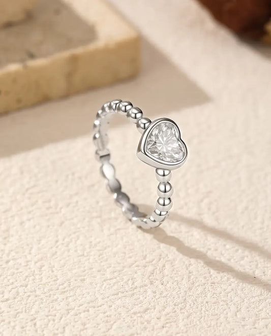 Bague Cœur Moissanite en Argent 925 - posée debout sur une surface claire texturée