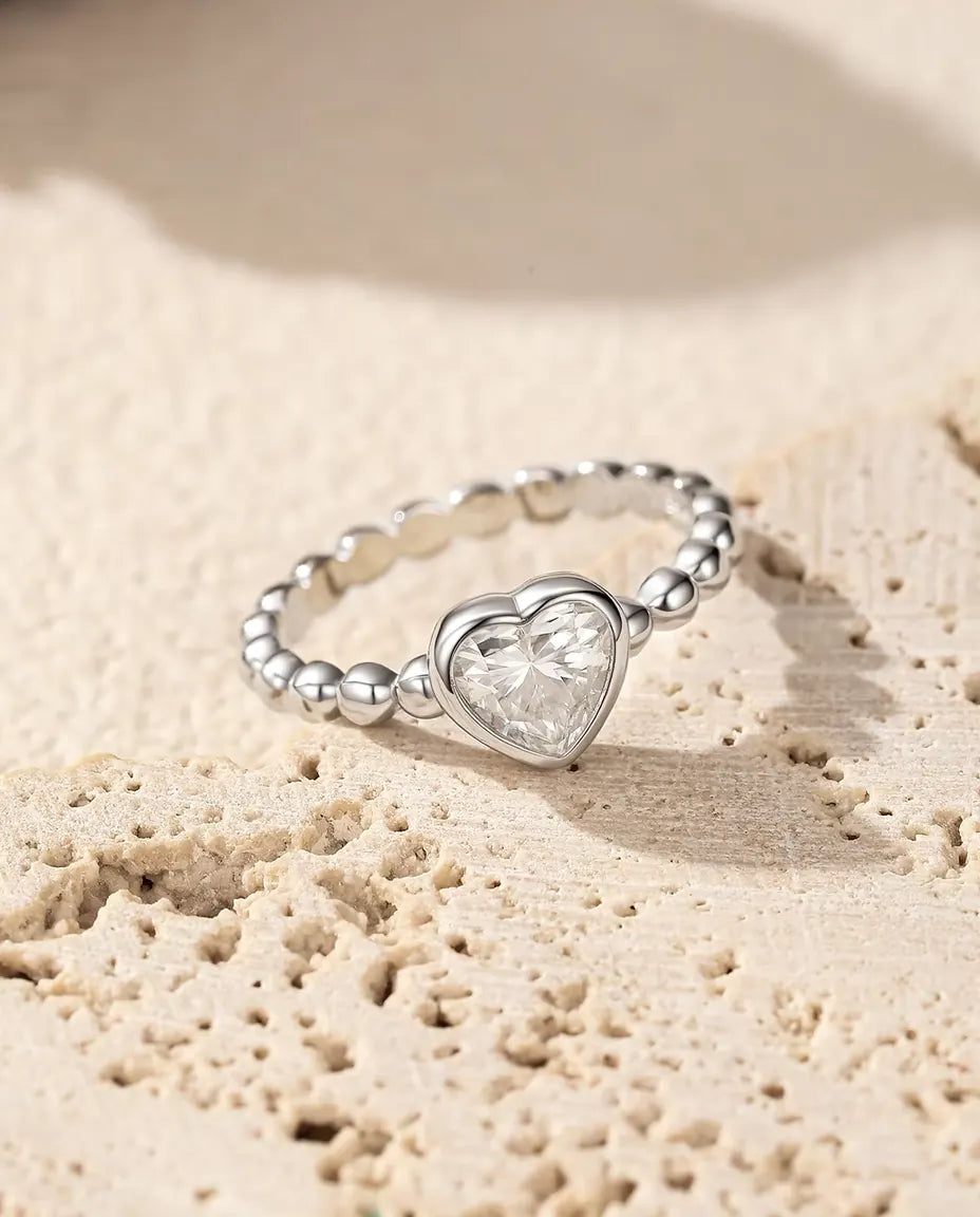 Bague Cœur Moissanite en Argent 925 - posée sur une surface de travertin poreux