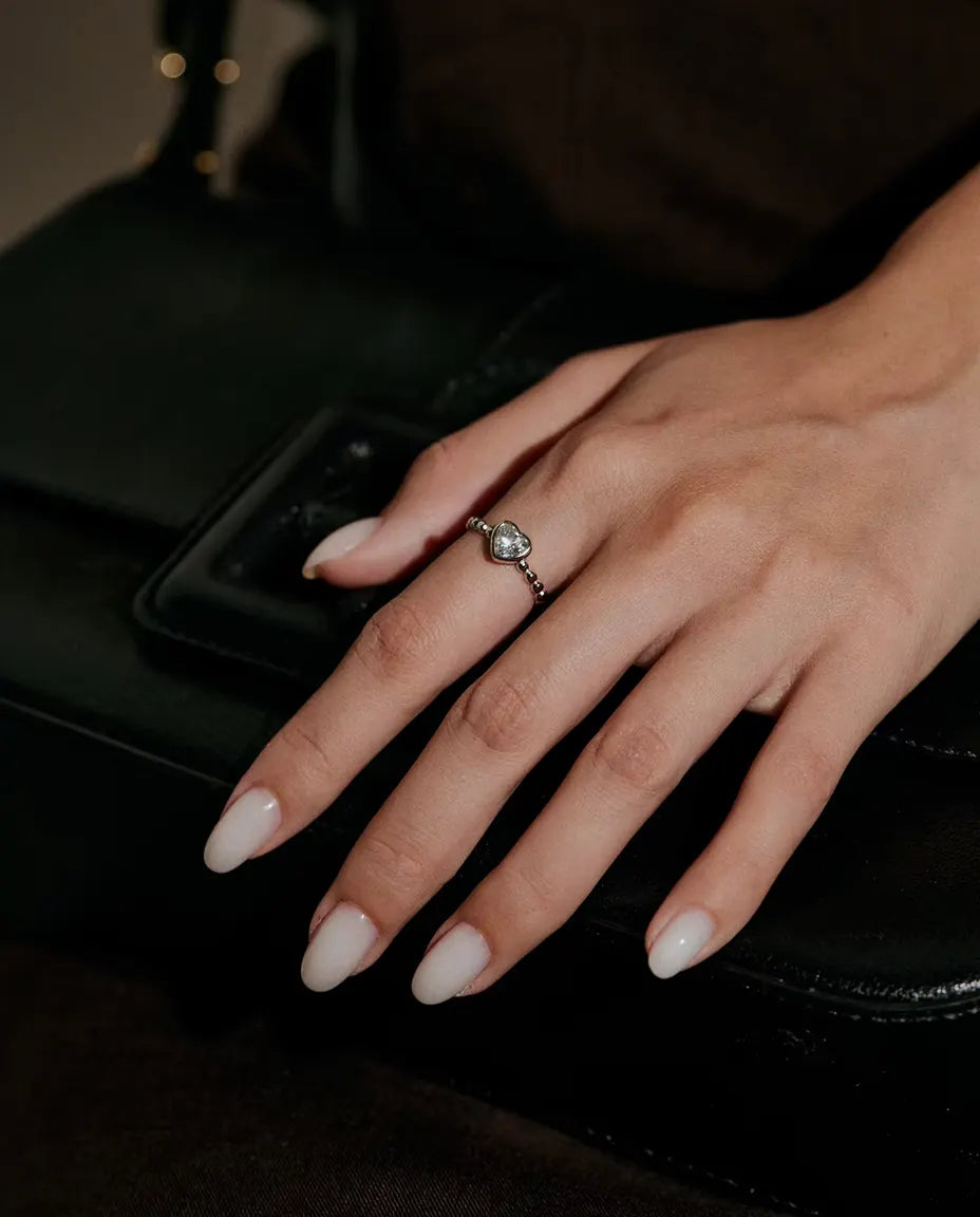 Bague Cœur Moissanite en Argent 925 - portée sur une main posée sur un sac noir