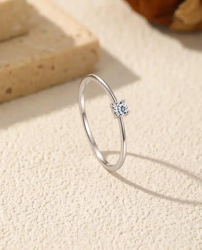 Bague Solitaire Moissanite Fine en Argent 925 - posée debout sur une surface claire texturée