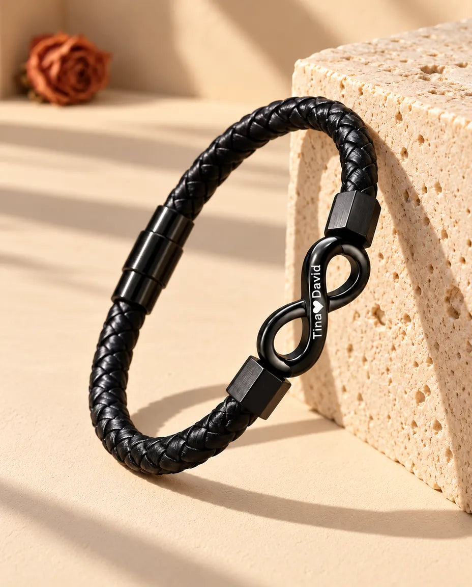Bracelet en similicuir tressé noir avec infini gravé, posé debout contre un bloc de travertin