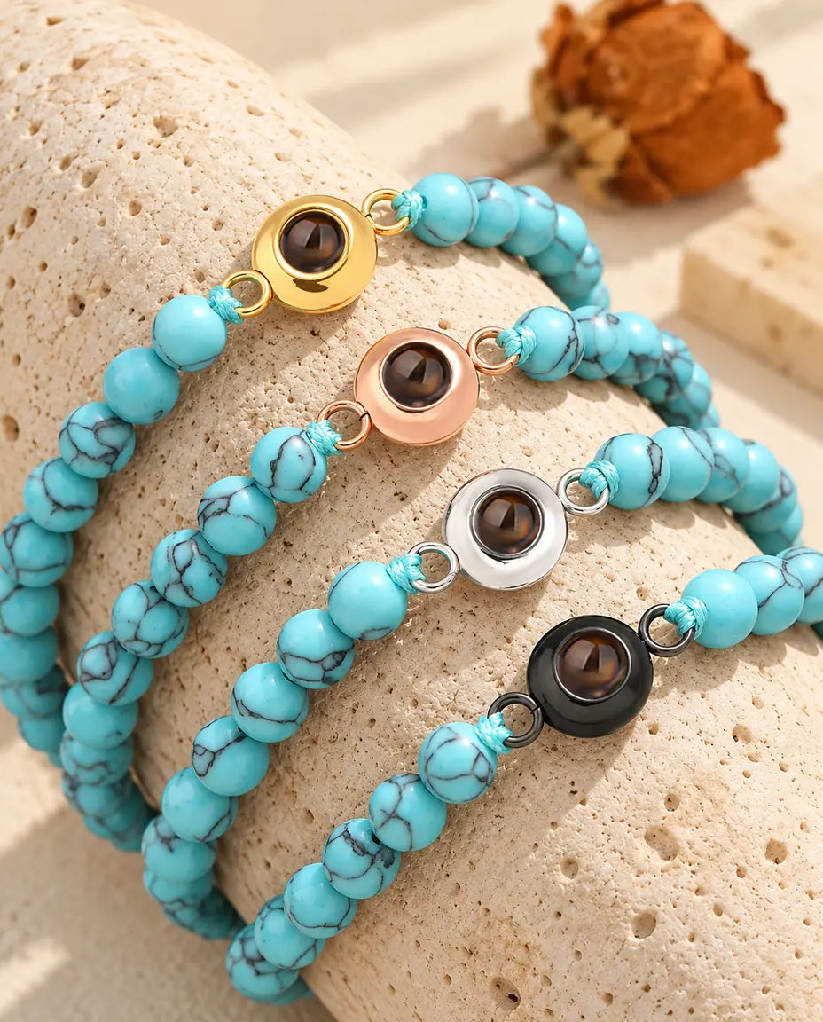 Quatre bracelets de perles bleu marbré avec charm doré, or rose, argenté et noir sur du travertin