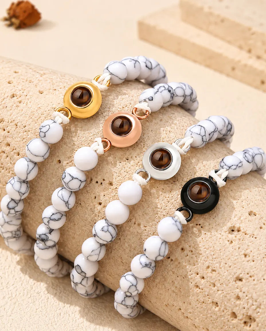 Bracelets de perles blanc marbré dans chaque couleur de charm sur un bloc de travertin