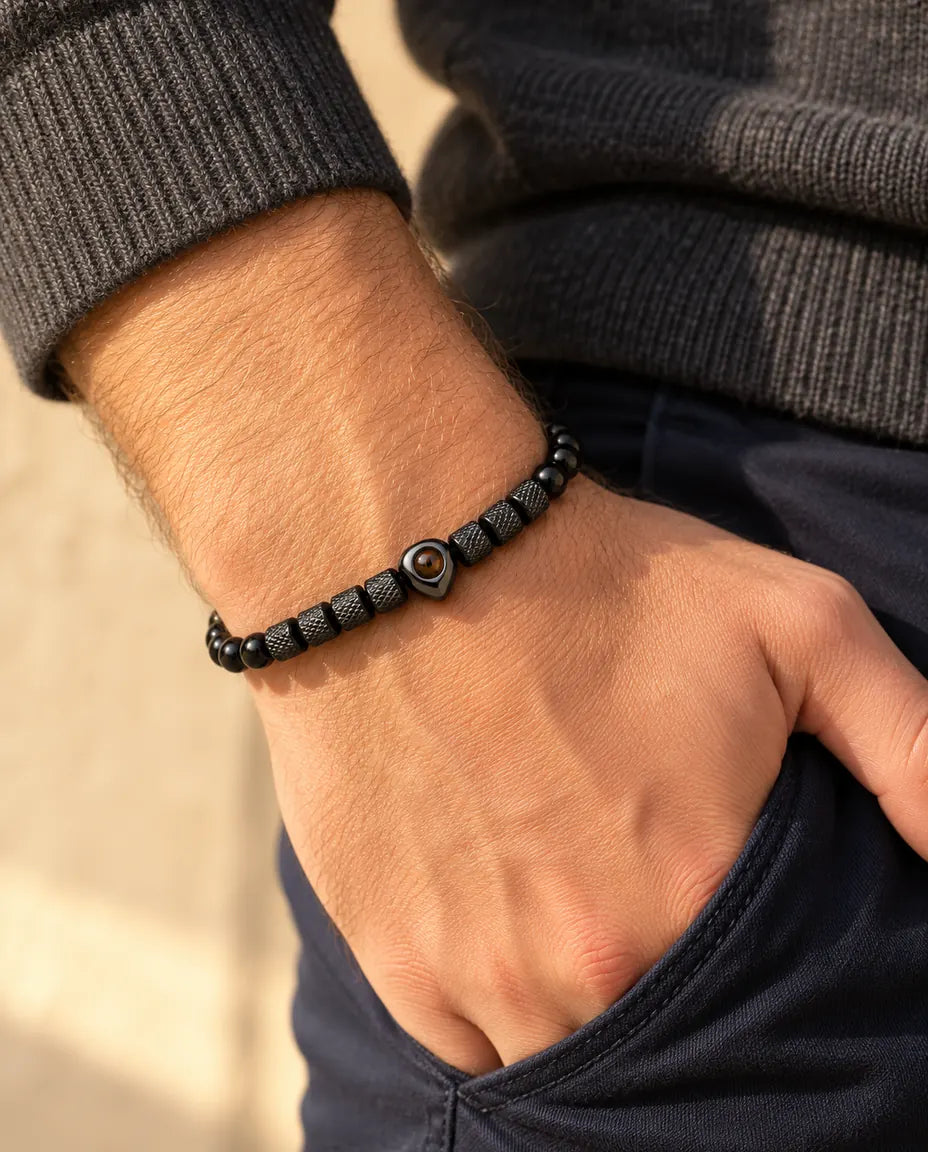 Homme portant le bracelet de perles noir à perle cœur, le pouce glissé dans sa poche