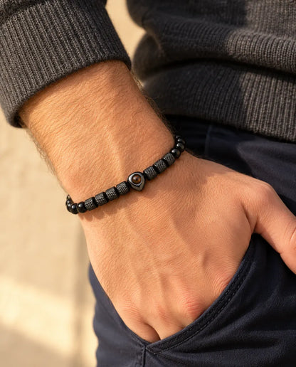 Homme portant le bracelet de perles noir à perle cœur, le pouce glissé dans sa poche