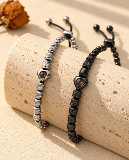 Bracelets de perles argenté et noir à perle cœur posés sur un bloc de travertin
