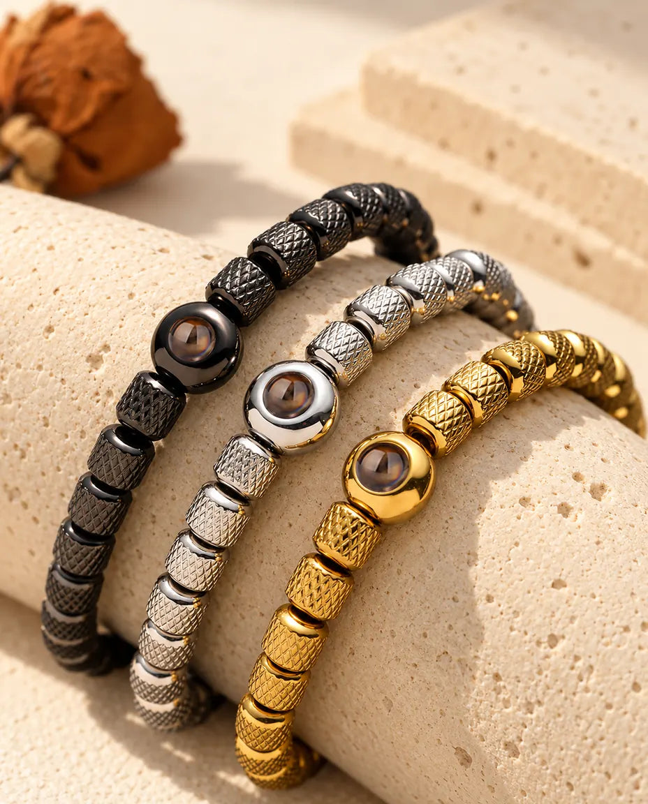 Trois bracelets de perles noir, argenté et doré posés sur un bloc de travertin