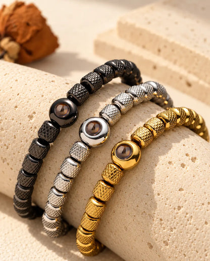Trois bracelets de perles noir, argenté et doré posés sur un bloc de travertin