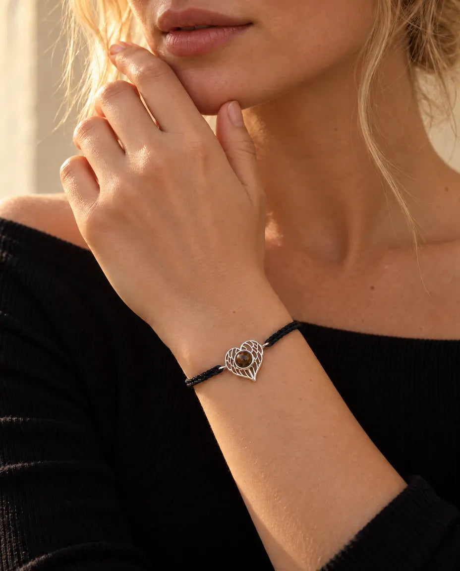Femme, les doigts au menton, portant le bracelet cœur ailes d'ange argenté sur cordon noir