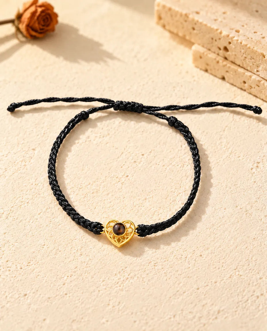 Vue de dessus du bracelet à cœur ajouré doré sur cordon fin tressé noir, nœud coulissant et brins