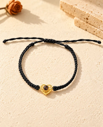 Vue de dessus du bracelet à cœur ajouré doré sur cordon fin tressé noir, nœud coulissant et brins