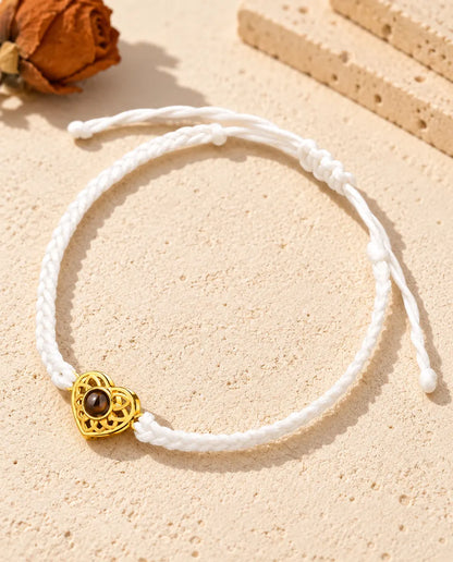 Bracelet cordon fin tressé blanc avec cœur ajouré doré et nœud coulissant sur plâtre clair