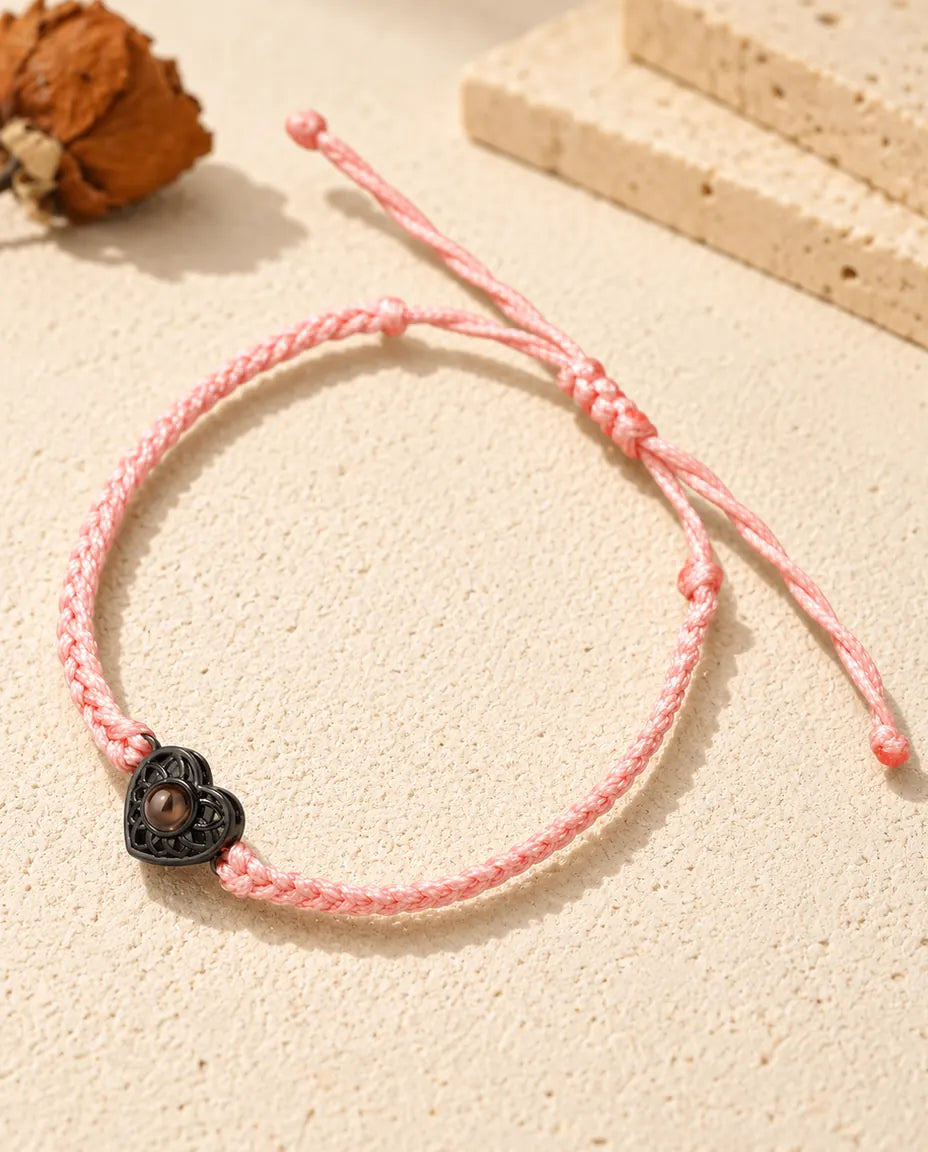 Bracelet cordon fin tressé rose avec cœur ajouré noir et pierre de projection brune sur plâtre