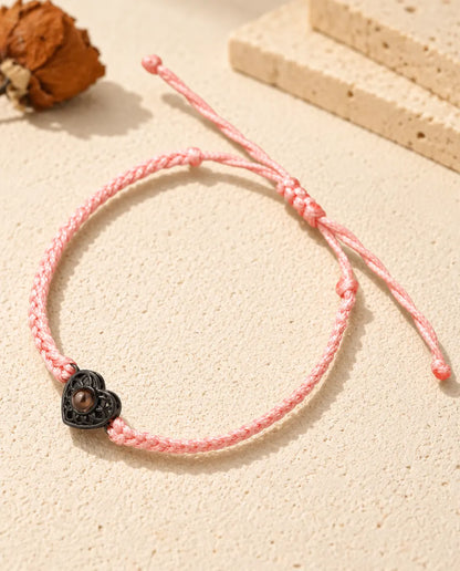 Bracelet cordon fin tressé rose avec cœur ajouré noir et pierre de projection brune sur plâtre