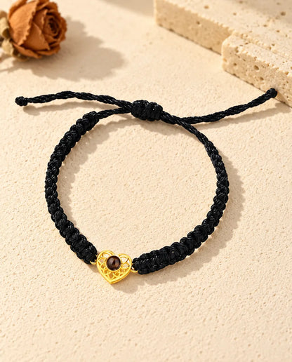 Vue de dessus du bracelet à cœur ajouré doré sur cordon tressé noir, nœud coulissant et brins