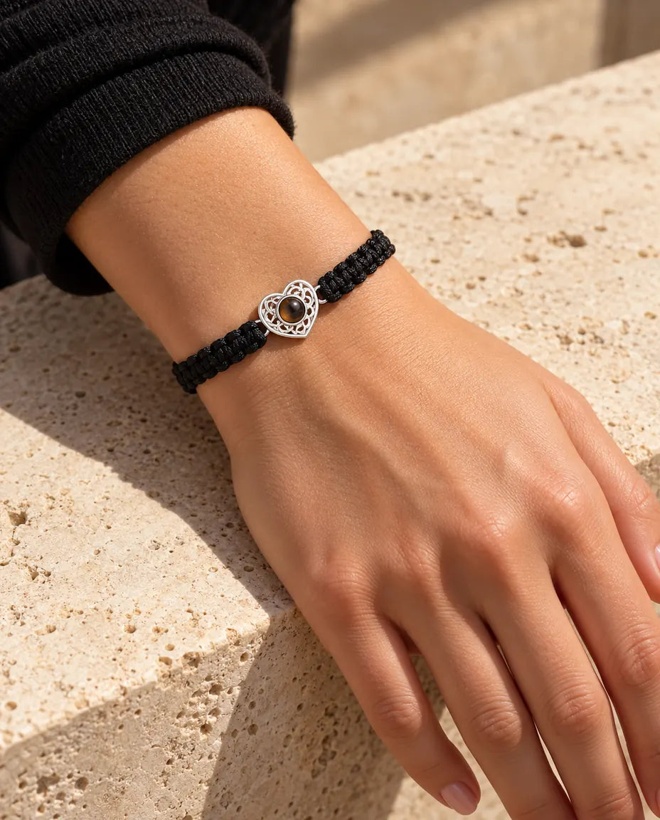 Femme portant le bracelet cordon tressé noir avec cœur ajouré argenté au poignet, sous une lumière chaude