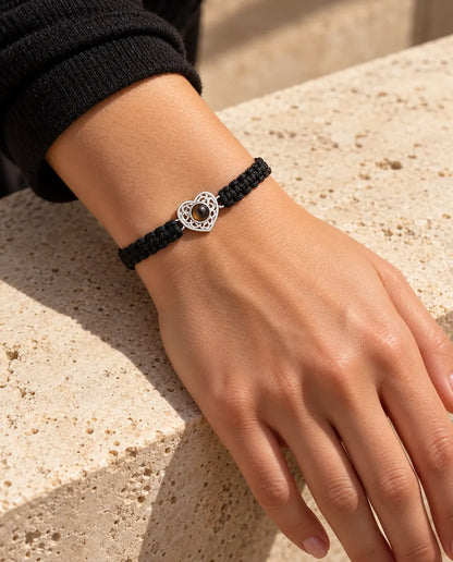 Femme portant le bracelet cordon tressé noir avec cœur ajouré argenté au poignet, sous une lumière chaude