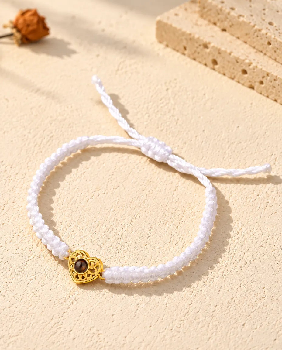 Bracelet cordon tressé blanc avec cœur ajouré doré et nœud coulissant sur plâtre clair
