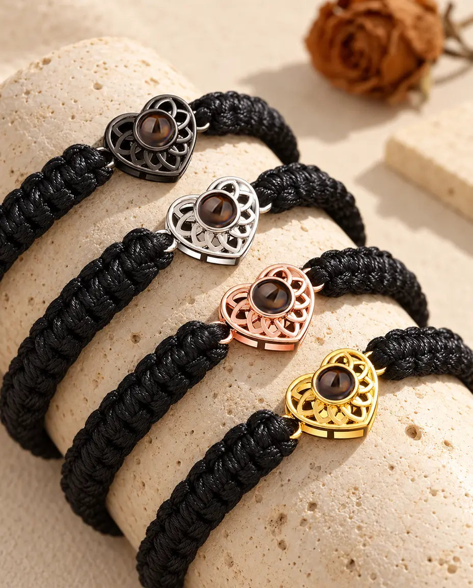 Quatre bracelets cordon tressé noir montrant chaque couleur de charm sur un bloc de travertin