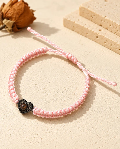 Bracelet cordon tressé rose avec cœur ajouré noir et pierre de projection brune sur plâtre