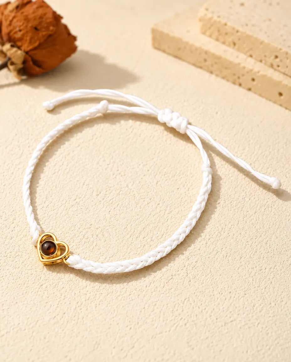 Bracelet cordon tressé blanc avec cœur ouvert doré et nœud coulissant sur plâtre clair