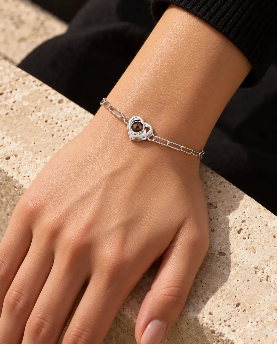 Femme portant le bracelet photo projection argenté double cœur au poignet, sous une lumière chaude