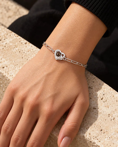 Femme portant le bracelet photo projection argenté double cœur au poignet, sous une lumière chaude