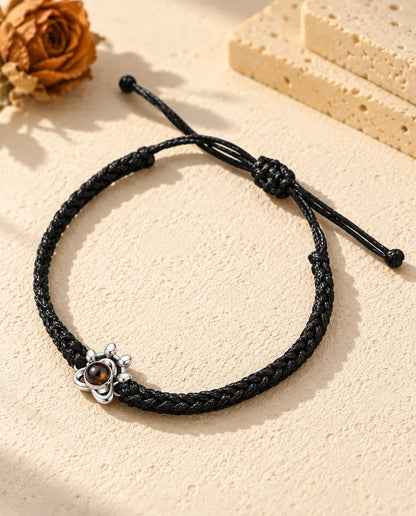 Bracelet photo projection : charm patte en argent 925 sur cordon tressé noir, posé sur plâtre clair