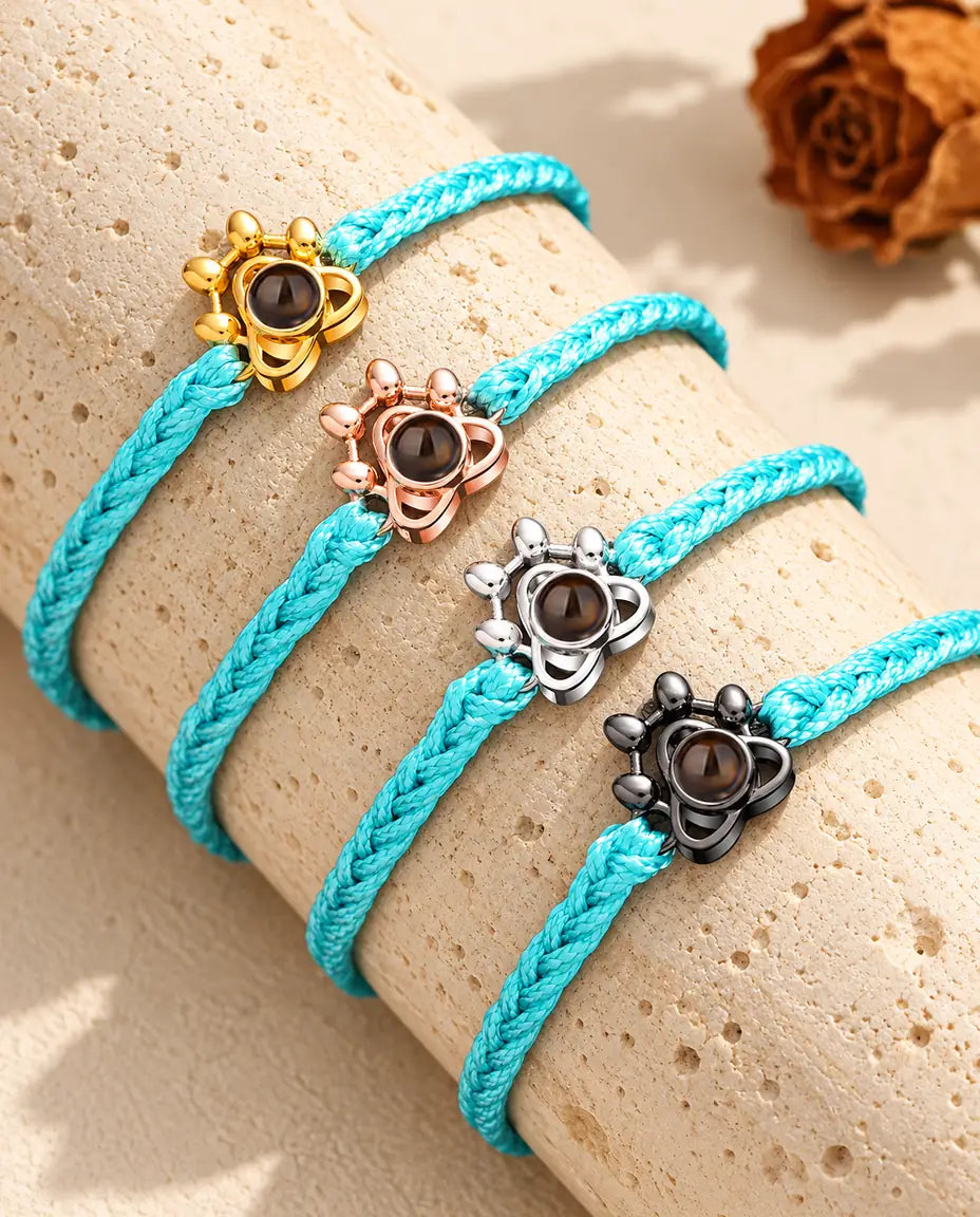 Quatre cordons tressés bleus avec charms patte doré, couleur or rose, argent et noir sur travertin