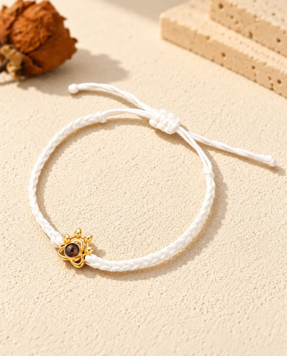 Bracelet cordon tressé blanc avec charm patte doré et nœud coulissant sur plâtre clair